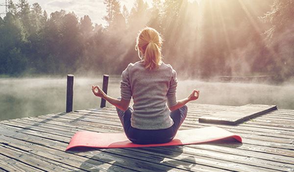 wellbeing, women sat on yoga mat outdoors by a lake or river